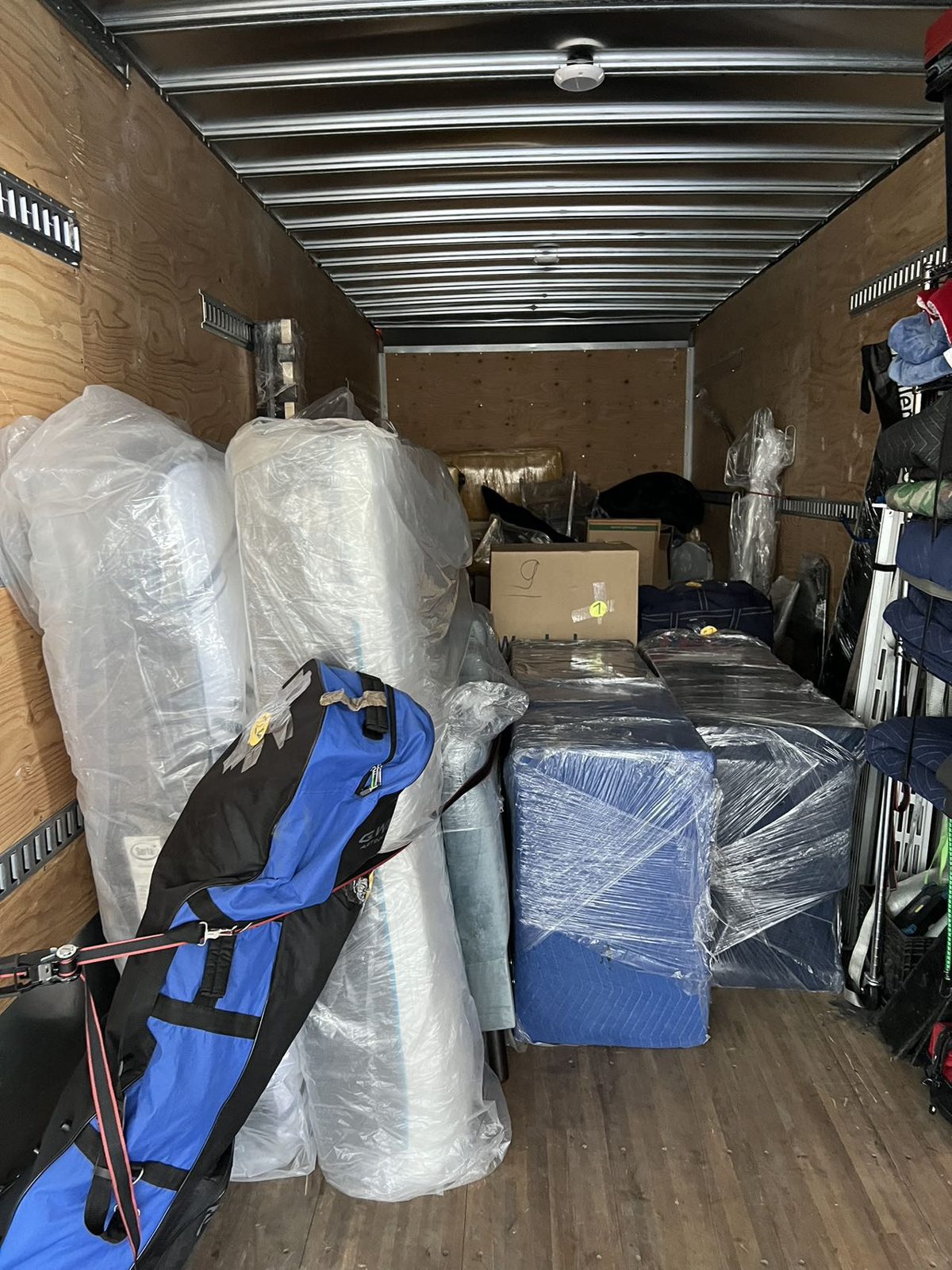 Moving truck loaded with plastic-wrapped mattresses and furniture tagged with colour room labels