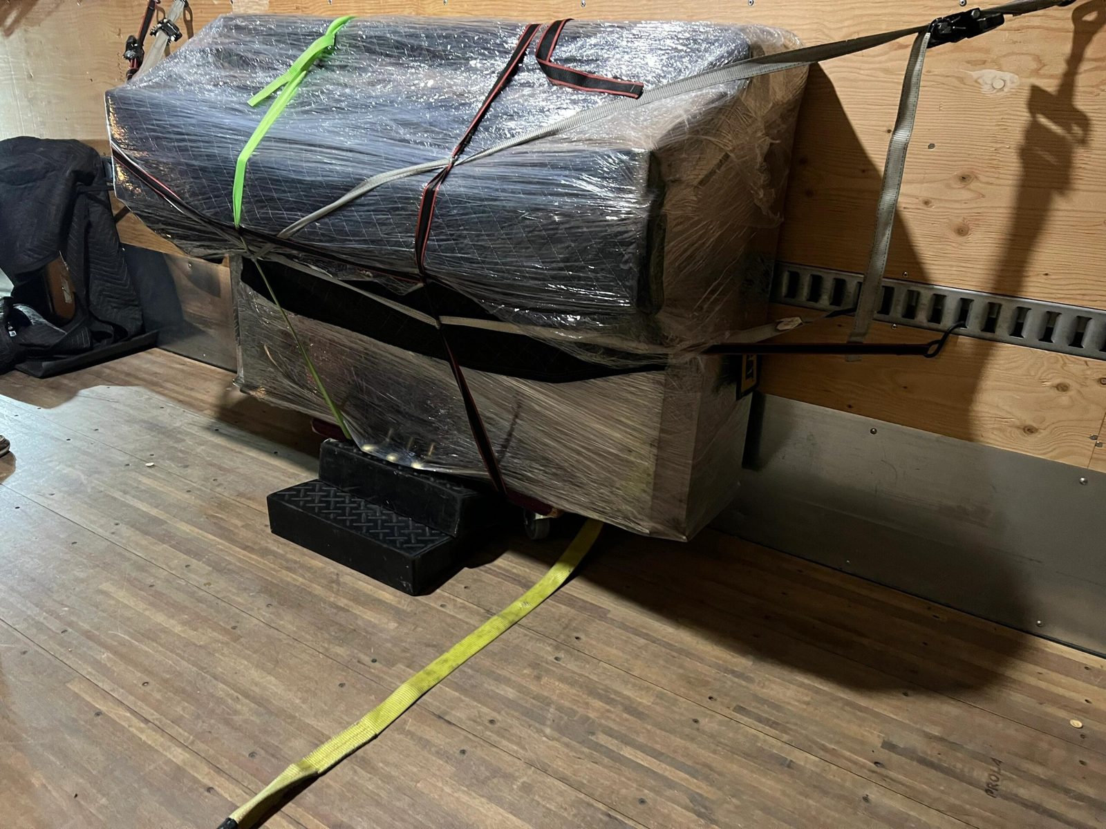 Upright piano wrapped, blocked and ratchet-strapped to the wall inside a moving truck